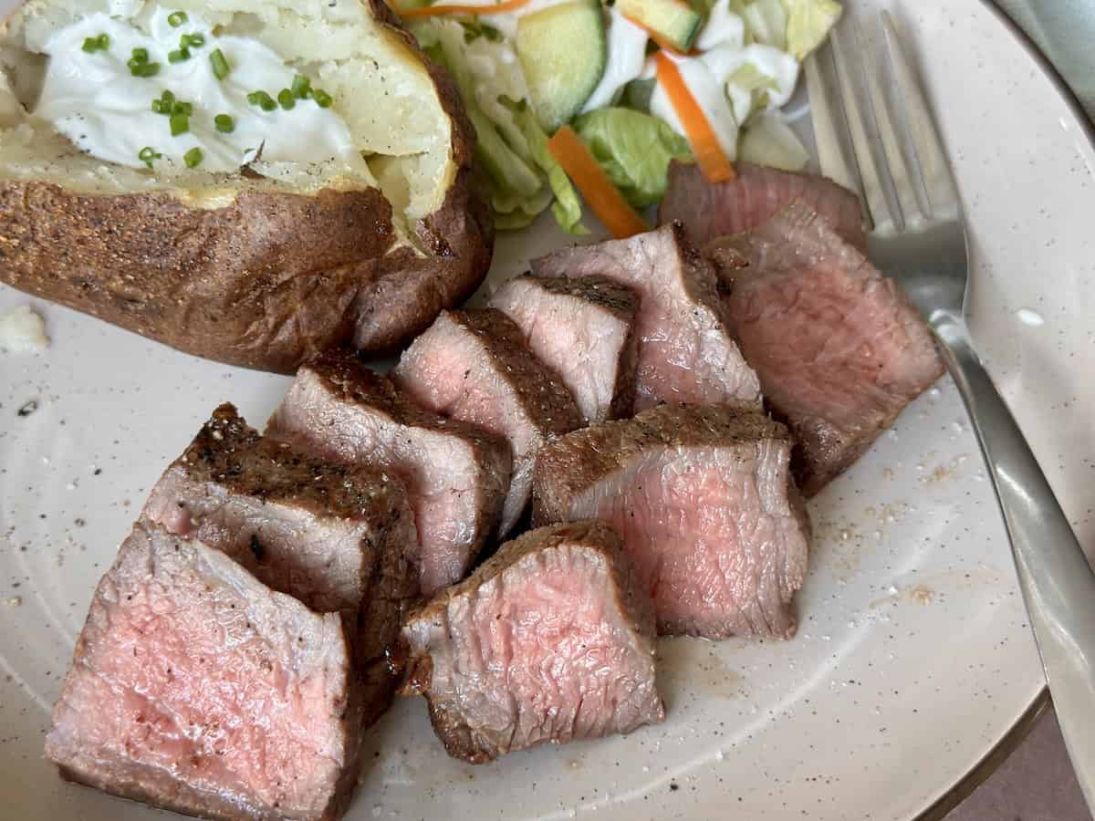 plate of sliced tri-tip steak with baked potato and salad