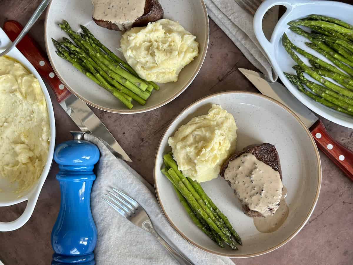 two steak dinners served on tan plates blue pepper grinder linens and cutlery