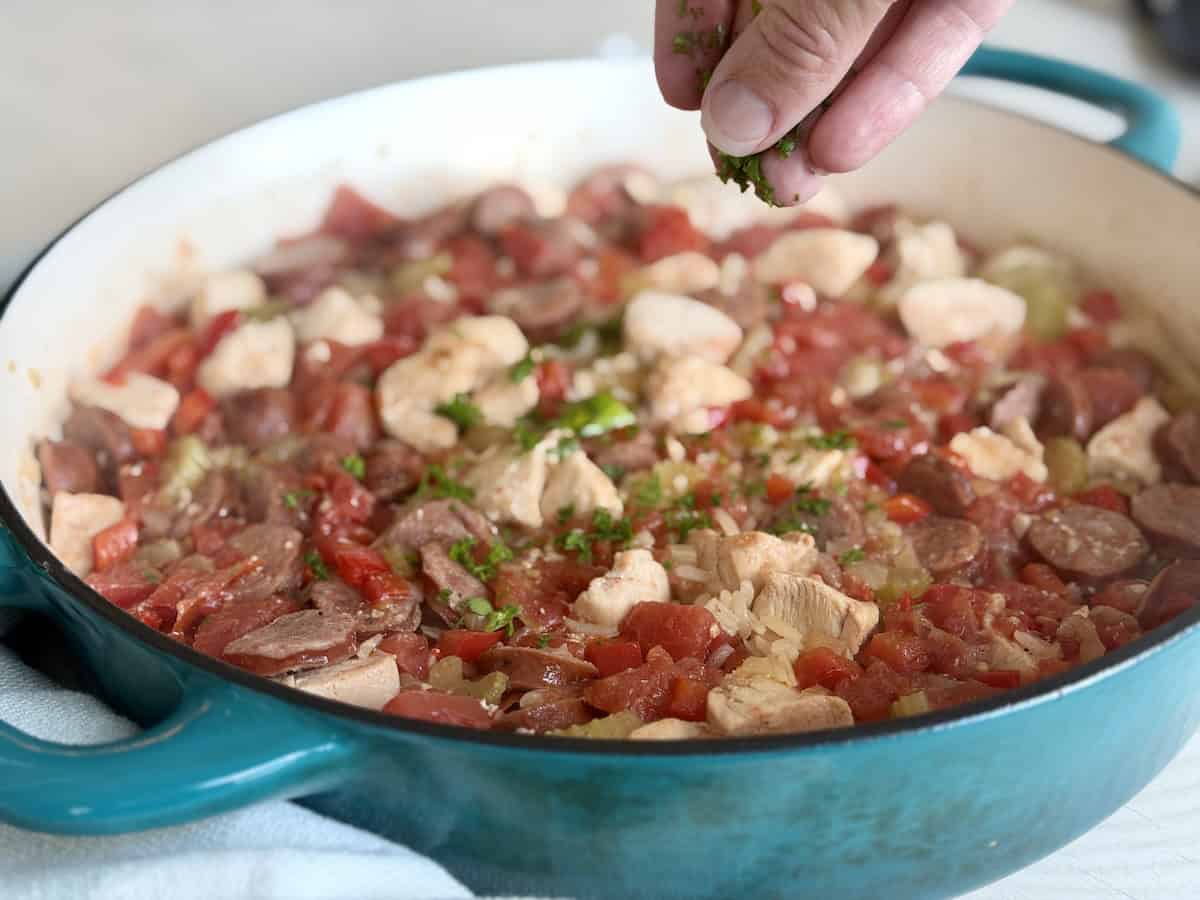 hand sprinkling chopped parsley over cooked jambalaya