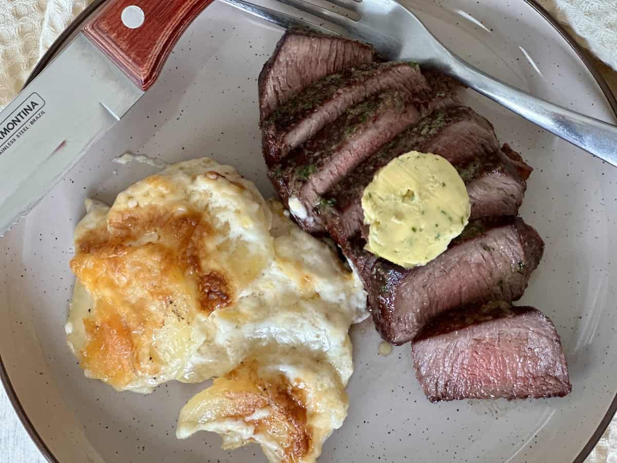 sleeks steak and au gratin potatoes on tan plate with steak knife and fork 