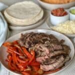 sliced fajita meat and red peppers on tan plate fajita toppings and tortillas