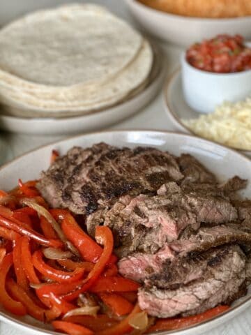 sliced fajita meat and red peppers on tan plate fajita toppings and tortillas