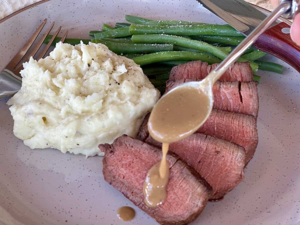 sliced steak with miso sauce on plate with green beans mashed potatoes 