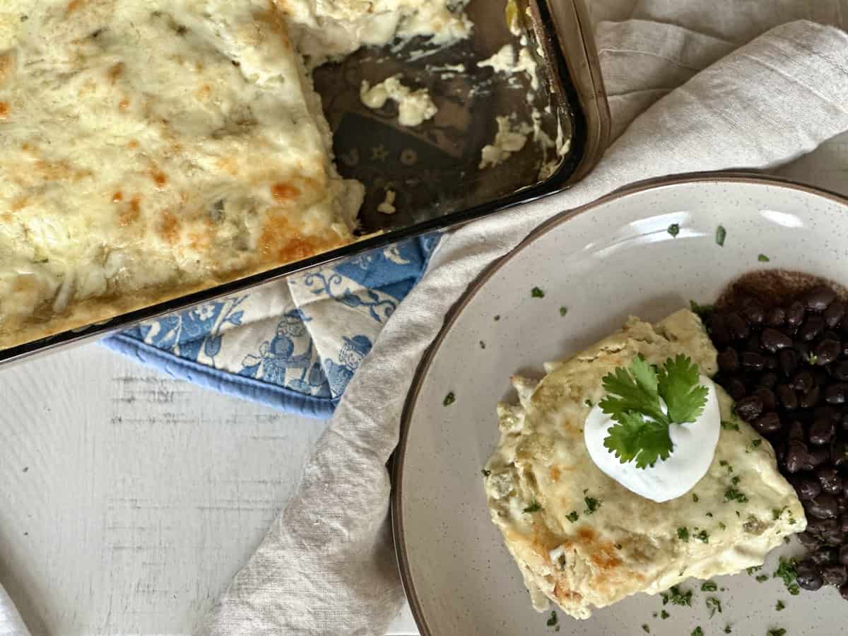 Sour cream enchilada casserole on a tan plate and in a glass baking dish.
