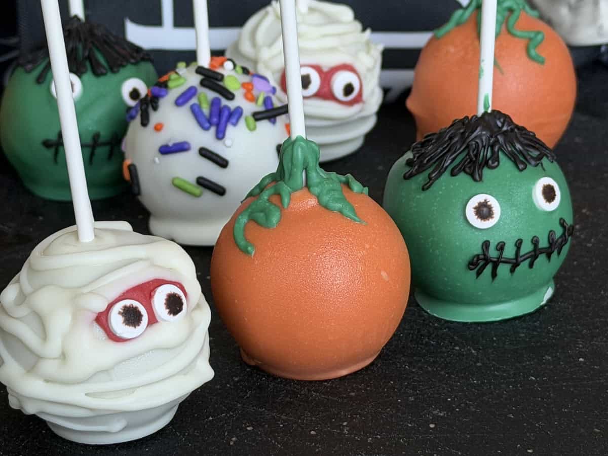halloween cake pops including a mummy pumpkin and master on black cutting board