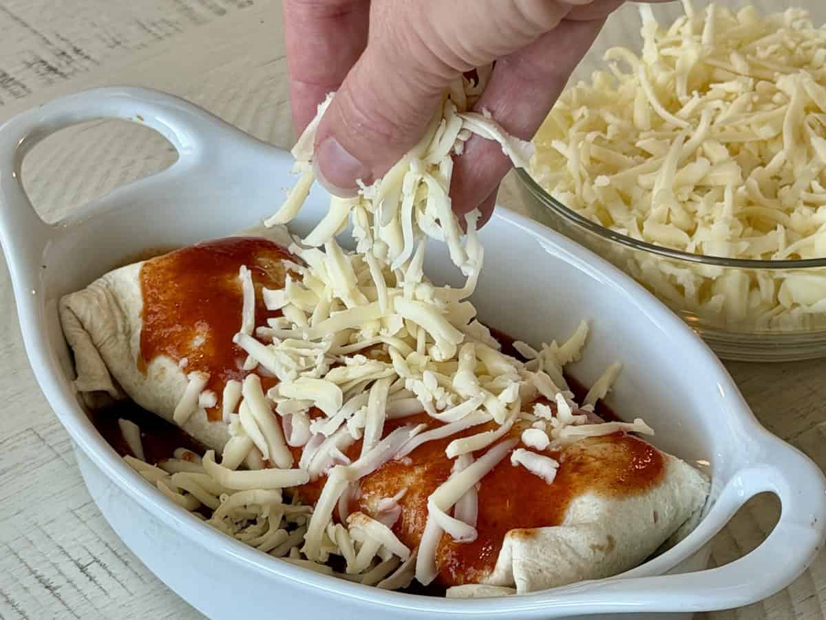 hand sprinkling cheese over top a saucy burrito