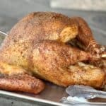 smoked whole turkey on baking sheet with tongs