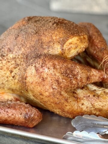 smoked whole turkey on baking sheet with tongs