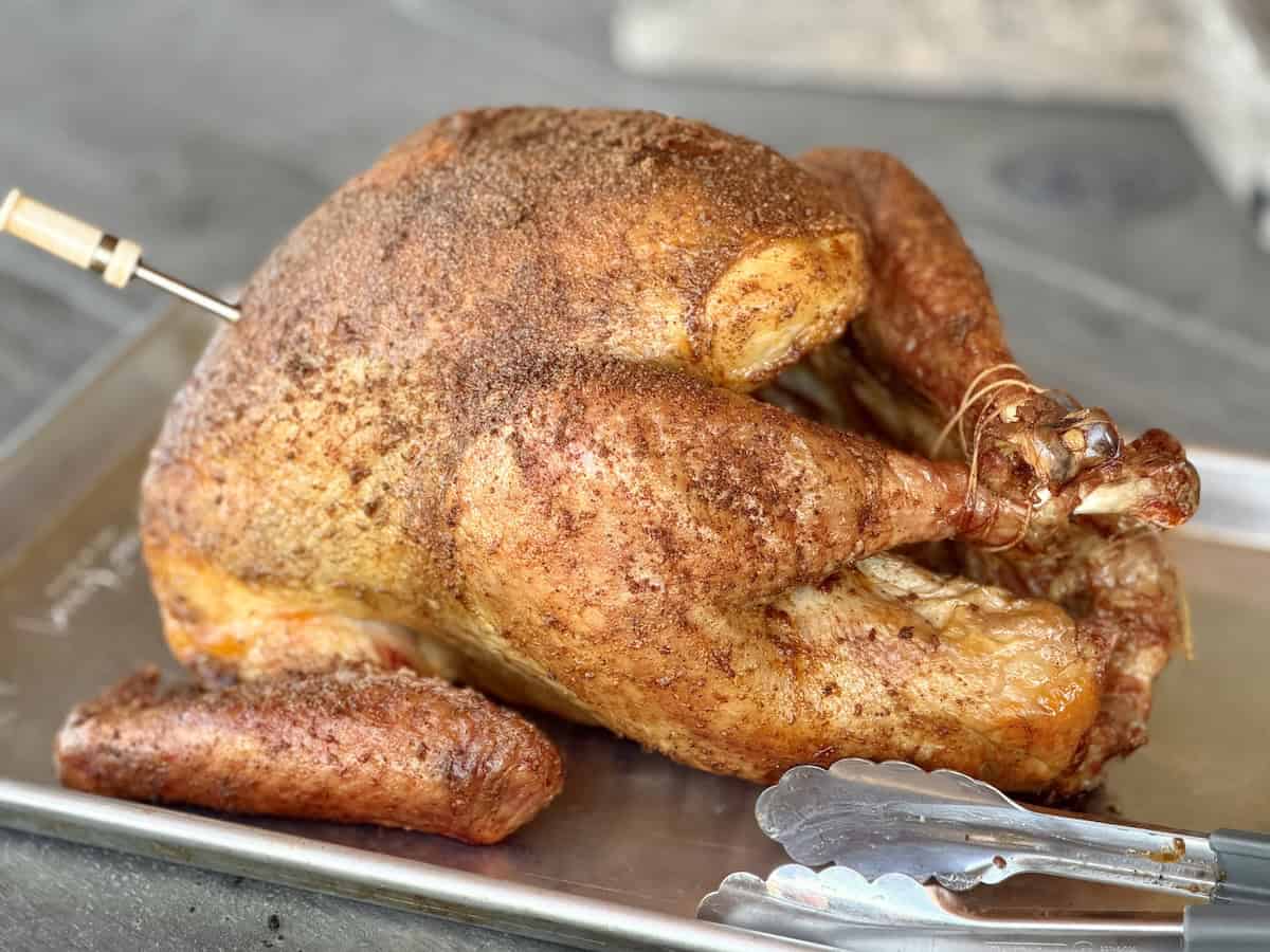 smoked whole turkey on baking sheet with tongs