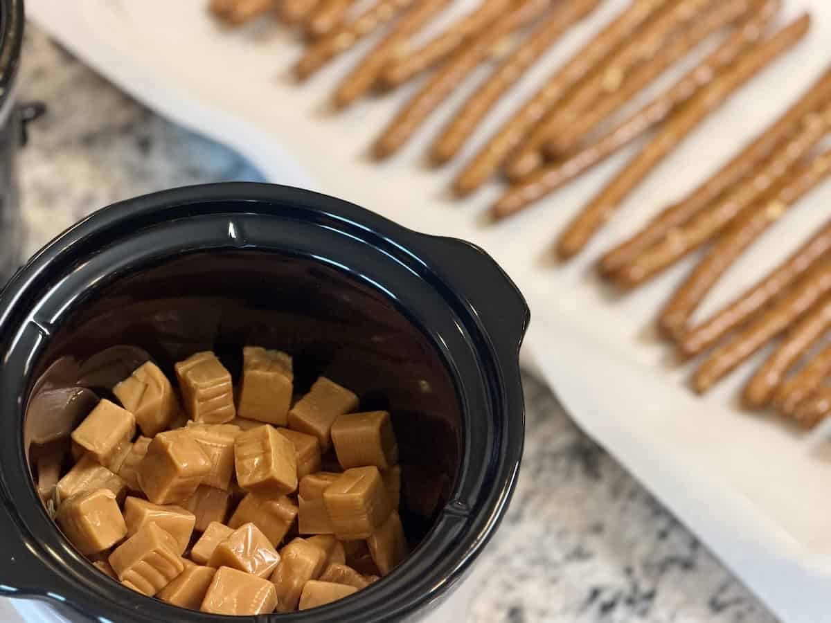 small crockpot with caramel cubes sheet pan with pretzel rods