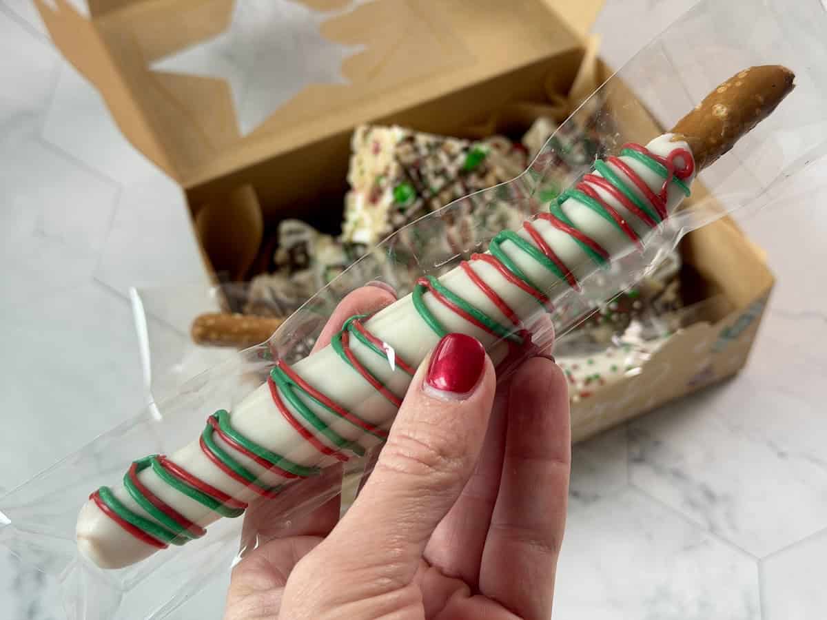 white chocolate dipped pretzel rod in plastic sleeve held in hand