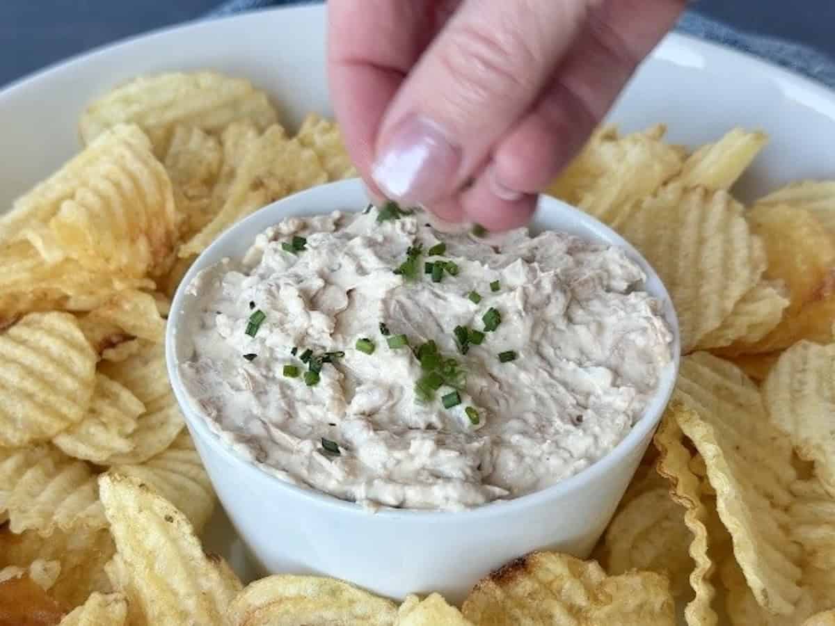 hand sprinkling chives on french onion dip