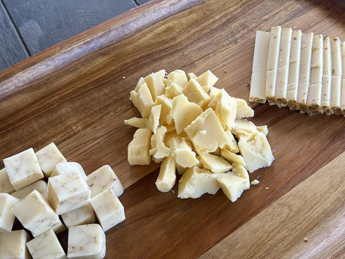 cheese cut into cubes broken into small chunks and thin rectangles on wood charcuterie board