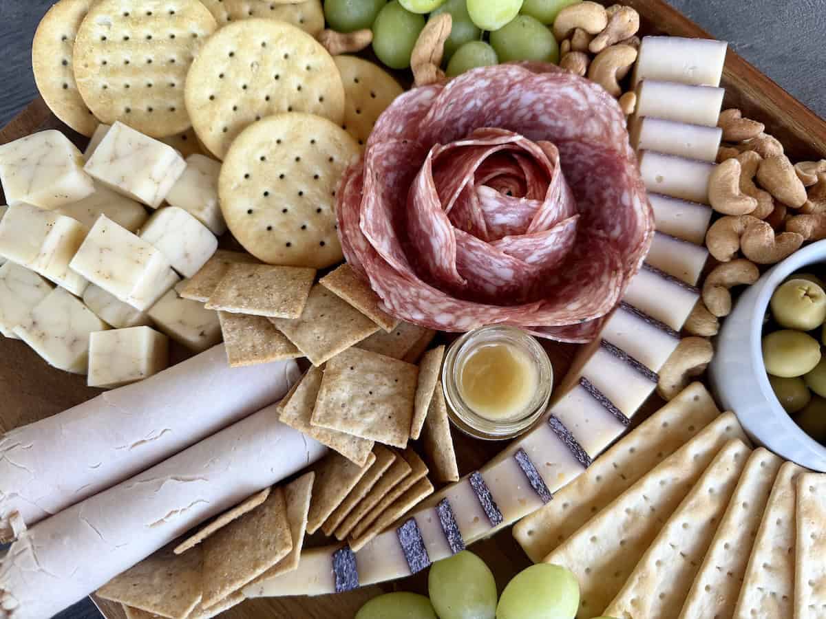 charcuterie board with crackers grapes salami and sliced cheese 