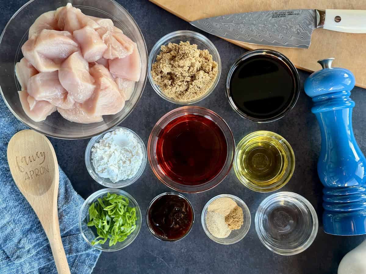 takeout bournon chicken ingredients in glass bowls blue background wood spoon cutting board and knife