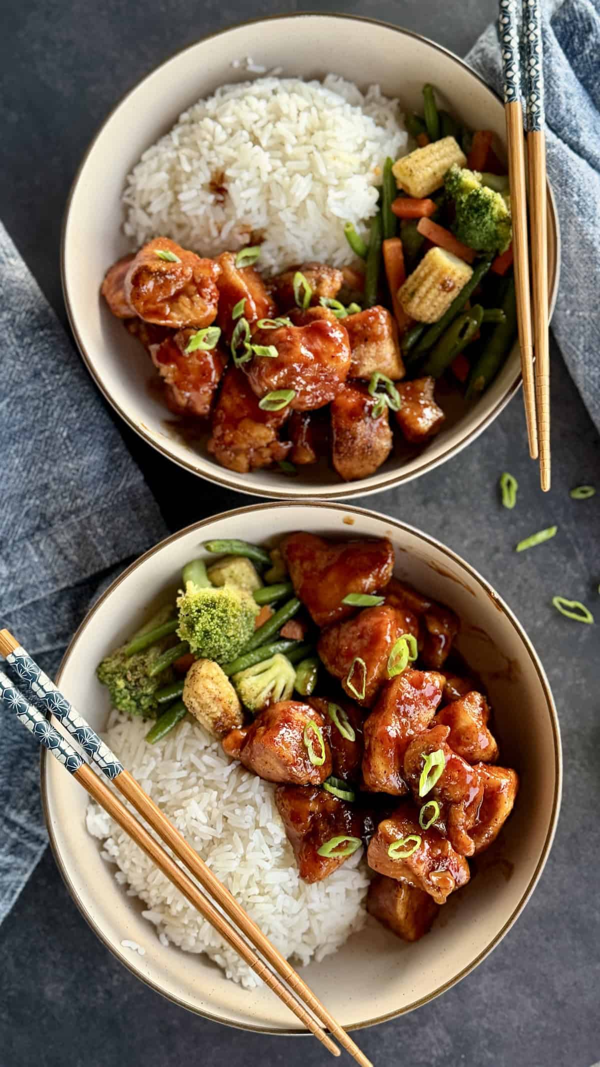 two bowls bourbon chicken with rive stir fried vegetables chopsticks blue napkins