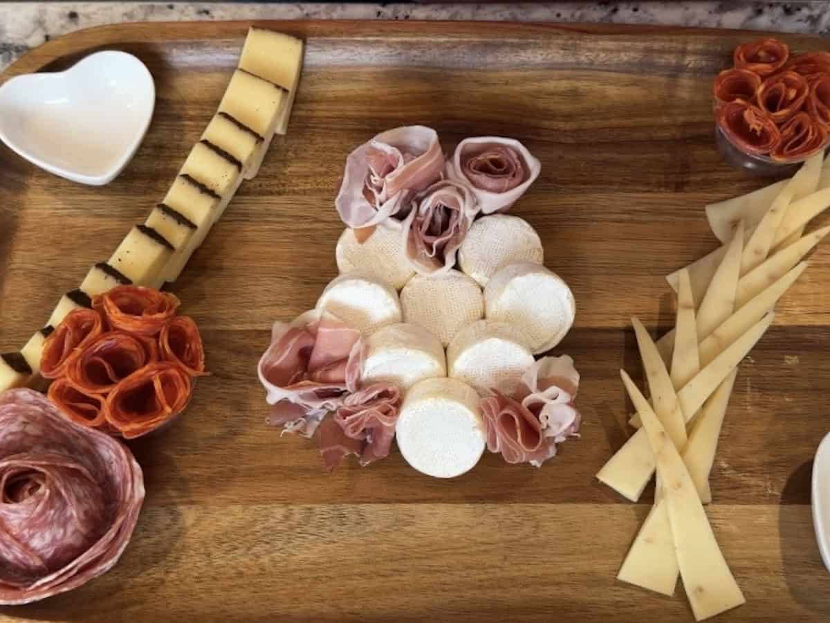wood board with salami roses cut cheese whit eheart shaped bowls