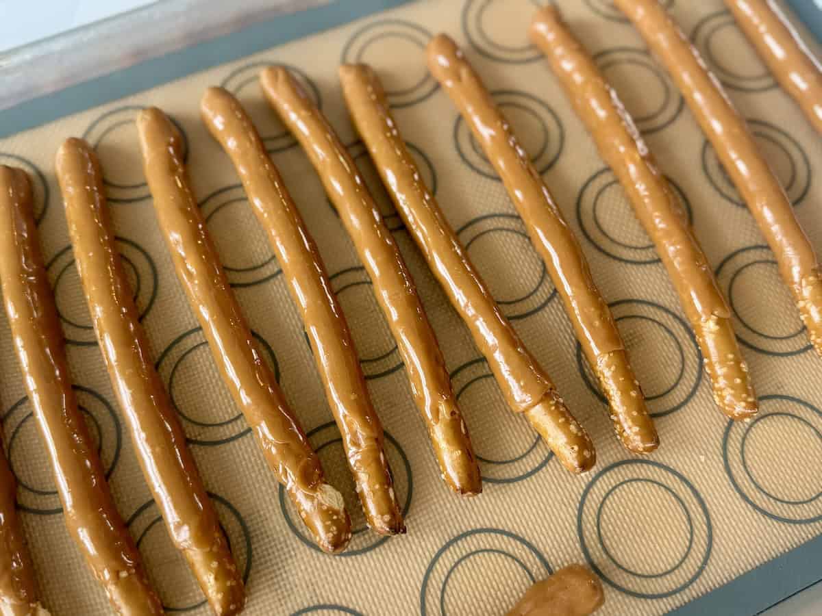 pretzel rods dipped in caramel on sheet pan lined with silpat