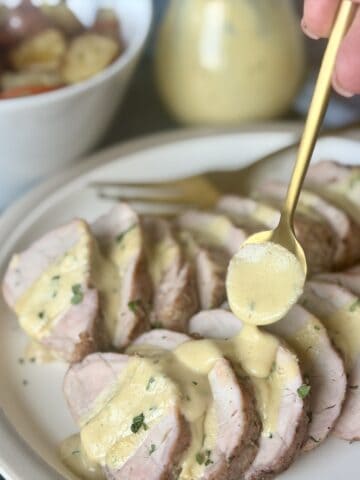gold spoon pouring mustard sauce over sliced pork tenderloin on white plate