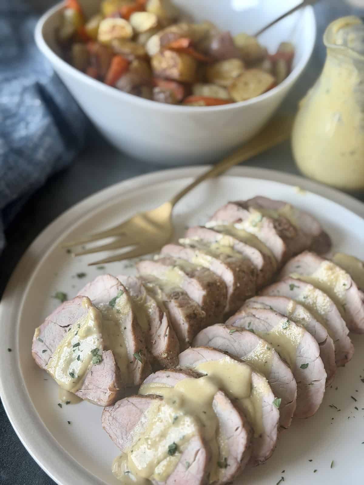 sliced pork tenderloin creamy mustard sauce on white plate roasted gold fork blue napkin vegetables