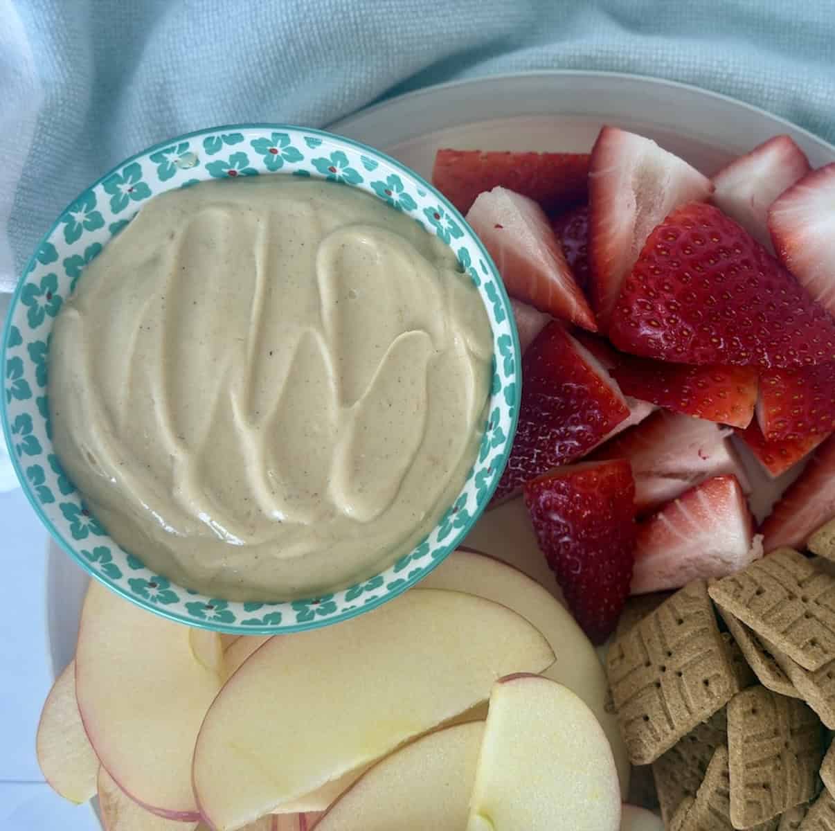 bowl of 4 ingredient peanut butter dip with cut strawberries sliced apples and graham crackers