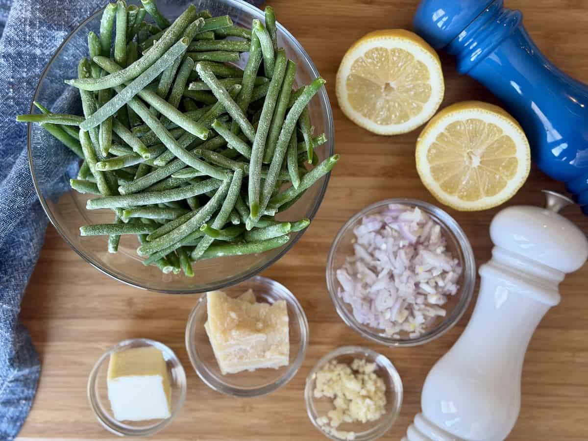 glass bowl frozen green beans lemon butter shallots garlic parmesan cheese salt and pepper grinder wood cutting board blue napkin