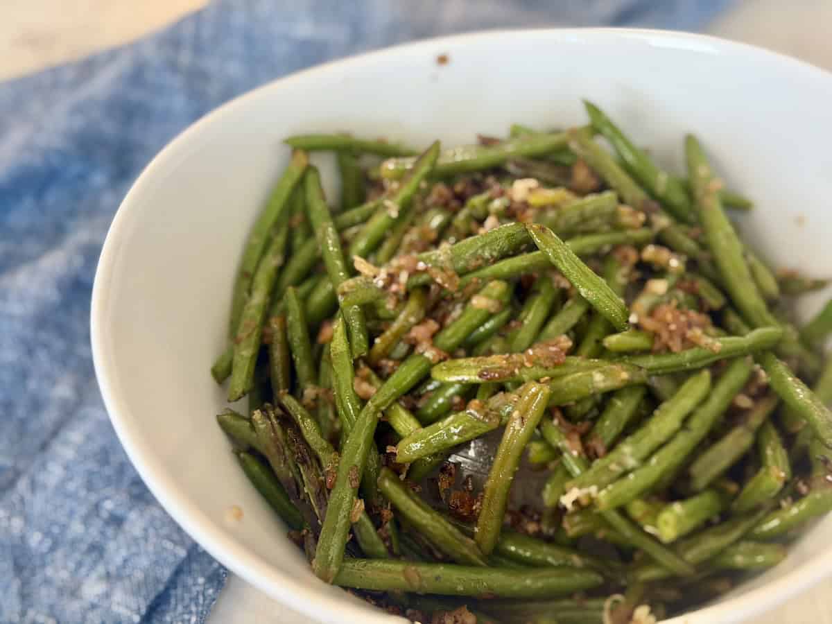 white serving bowl of cooked green beans with carmelized shallots and parmesan cheese blue napkin 