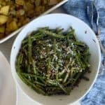 white bowl of cooked green beans blue napkin serving tongs white dish of potatoes
