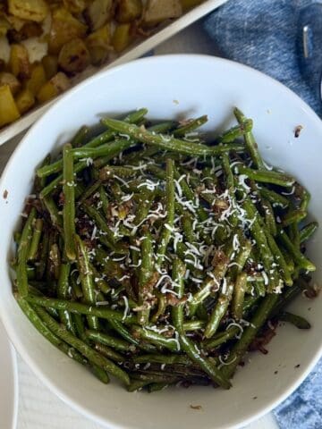 white bowl of cooked green beans blue napkin serving tongs white dish of potatoes