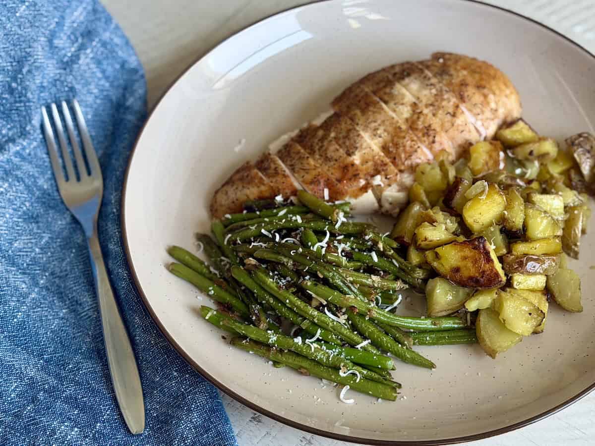 sliced chicken roast potatoes and green beans on tan plat with fork and blue napkin