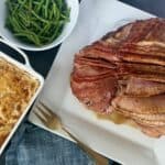 cooked spiral ham on white plate white bowl of green beans baking dish of au gratin potatoes