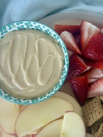 bowl of 4 ingredient peanut butter dip with cut strawberries sliced apples and graham crackers