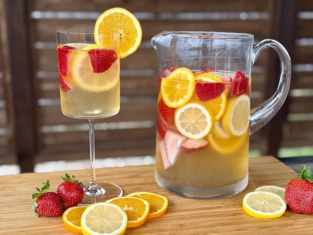 glass pitcher of white wine sangria glass of sangria sliced oranges lemons and strawberries