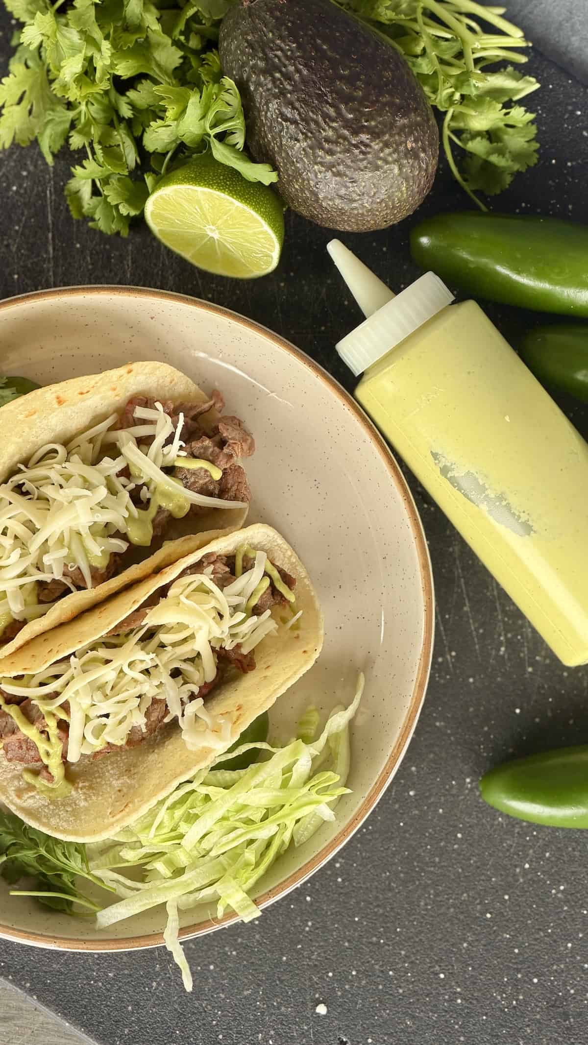 two steak tacos tan plate bottle of taco sauce avocado lime cilantro on cutting board