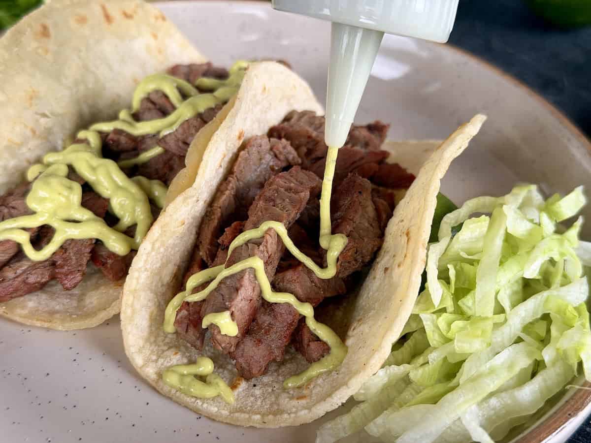 pouring green taco sauce onto two tacos brown plate
