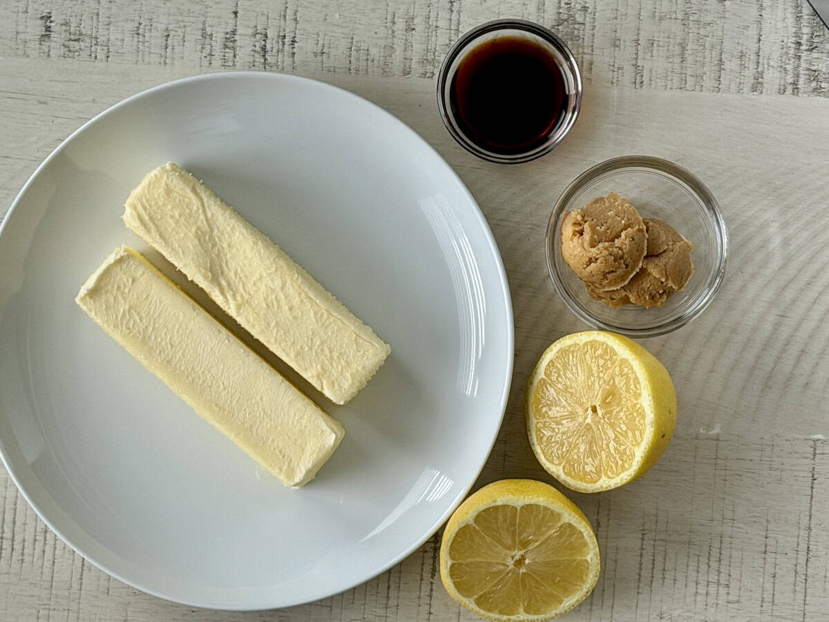 two sticks butter on white plate glass bowls of soy sauce, miso paste and lemon cut in half