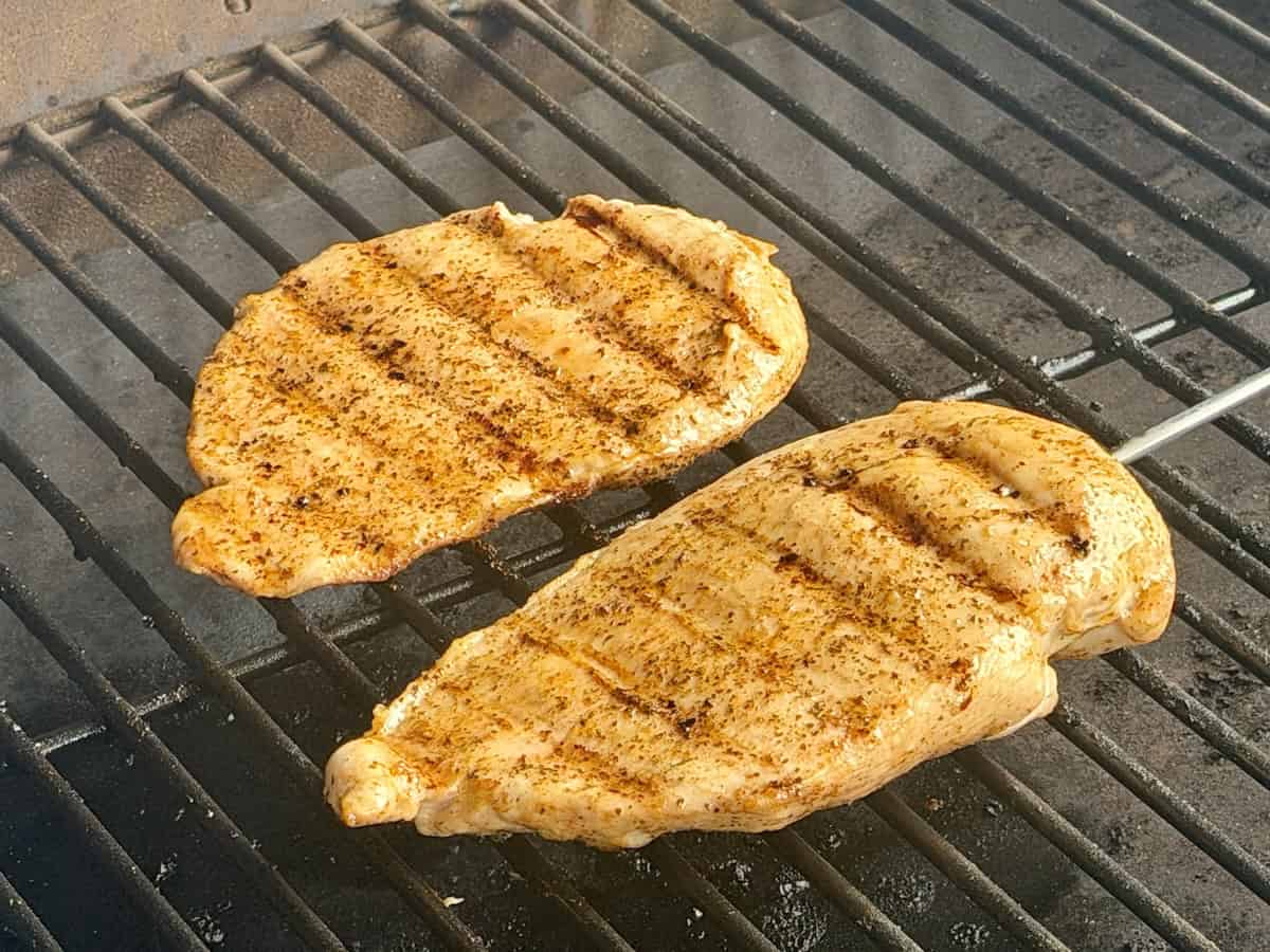 two chicken breasts cooking on grill grates