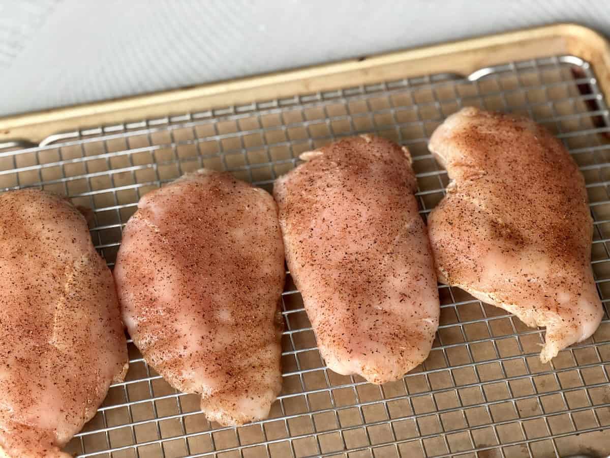 4 seasoned chicken breasts on a sheet pan lined with a wire rack