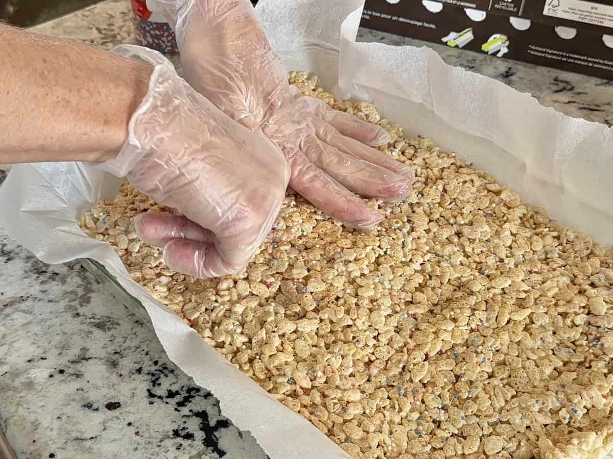 hand pressing Rice Krispies treats in baking dish