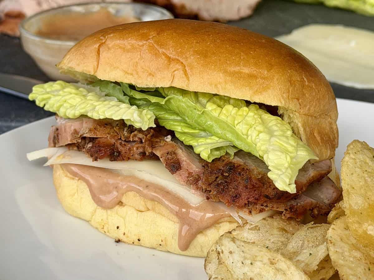 pork tenderloin sandwich on white plate potato chips