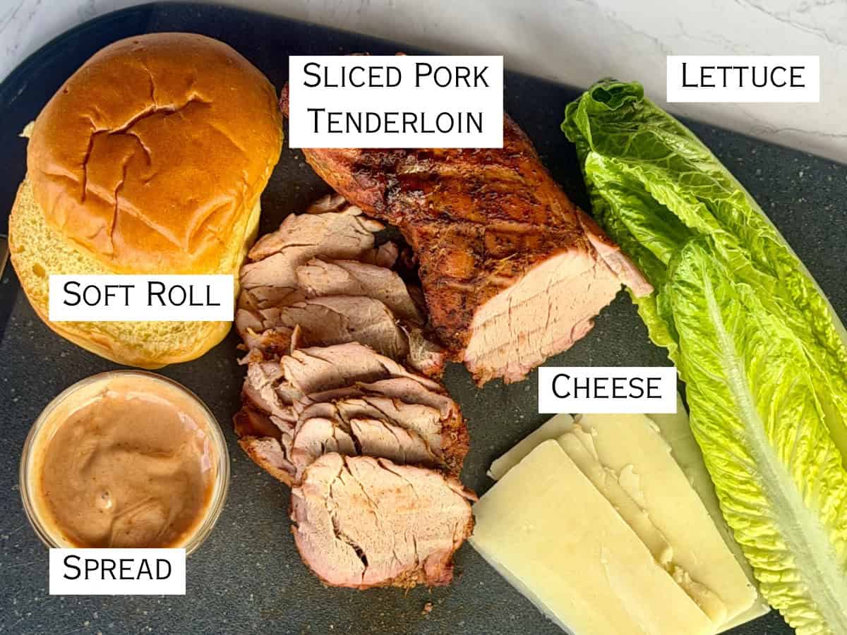 soft roll sliced pork tenderloin romaine lettuce spread sliced white cheese black cutting board
