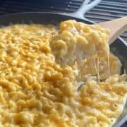 wooden spoon scooping smoked Macaroni and cheese from cast iron pan on grill