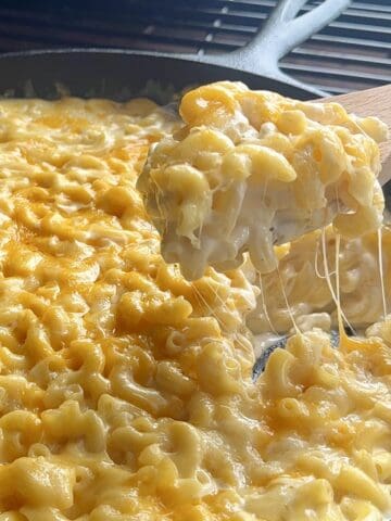 wooden spoon scooping smoked Macaroni and cheese from cast iron pan on grill