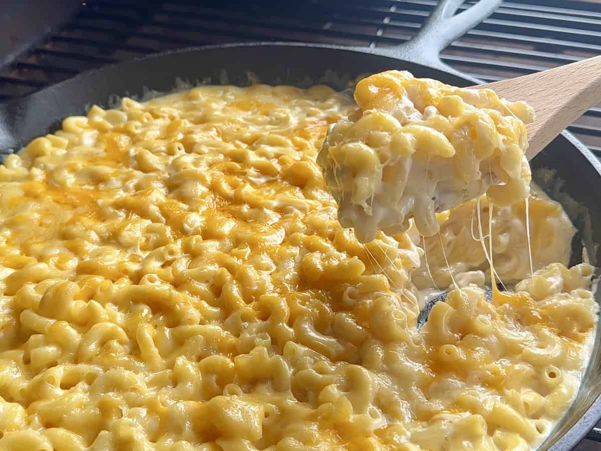 wooden spoon scooping smoked Macaroni and cheese from cast iron pan on grill