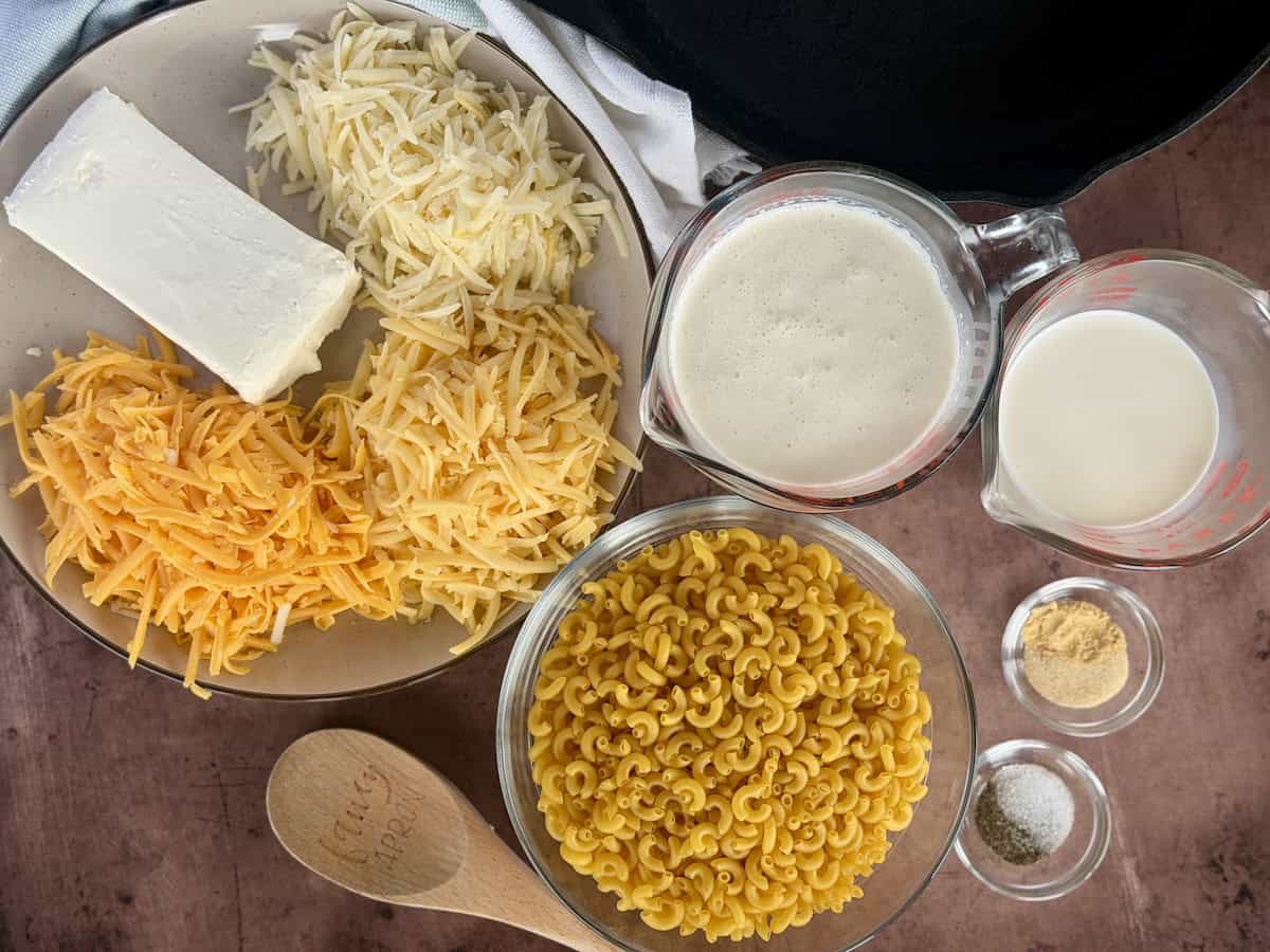 tan plated of shredded cheese and cream cheese elbow pasta shells cream spices in glass bowls wood spoon