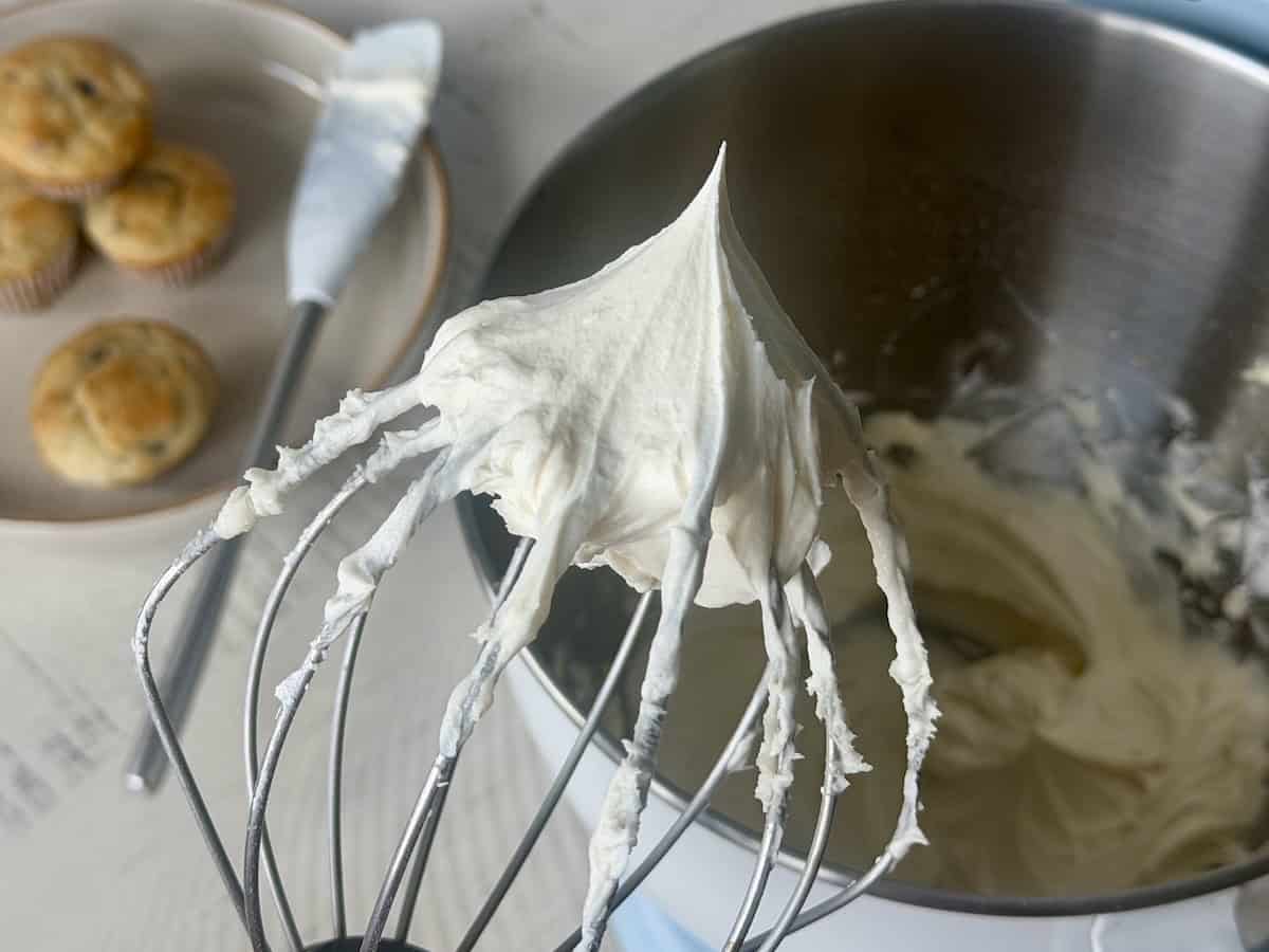 whisk attachment from stand mixer with whipped frosting and mixing bowl