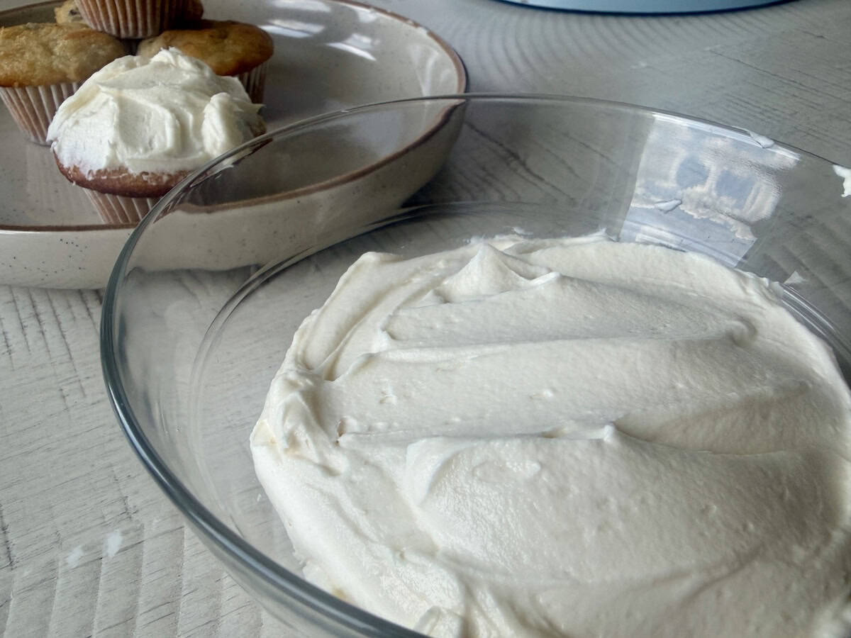 glass bowl of homemade vanilla frosting and mini muffins on plate