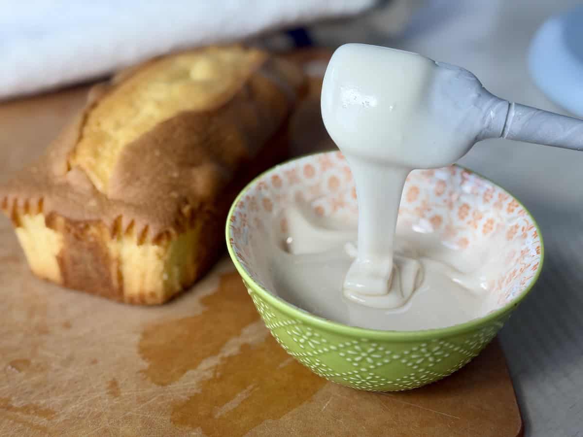 3 ingredient icing in green bowl pouring off spatula loaf cake on cutting board