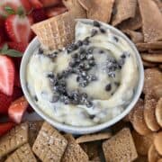 cannoli dip in bowl topped with chocolate chips waffle cone pieces cut strawberries and cookies for dipping