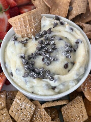cannoli dip in bowl topped with chocolate chips waffle cone pieces cut strawberries and cookies for dipping